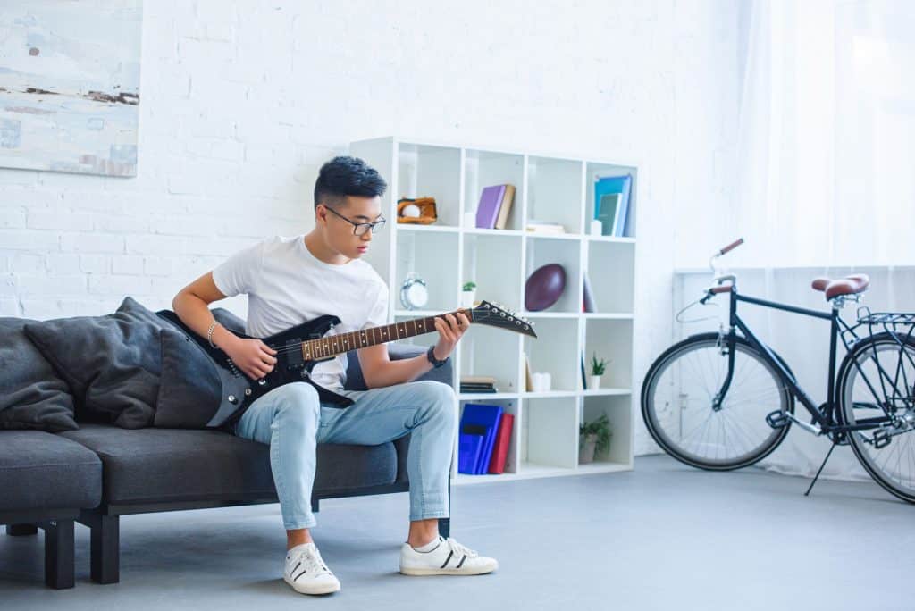 Asian man playing black electric guitar in his room