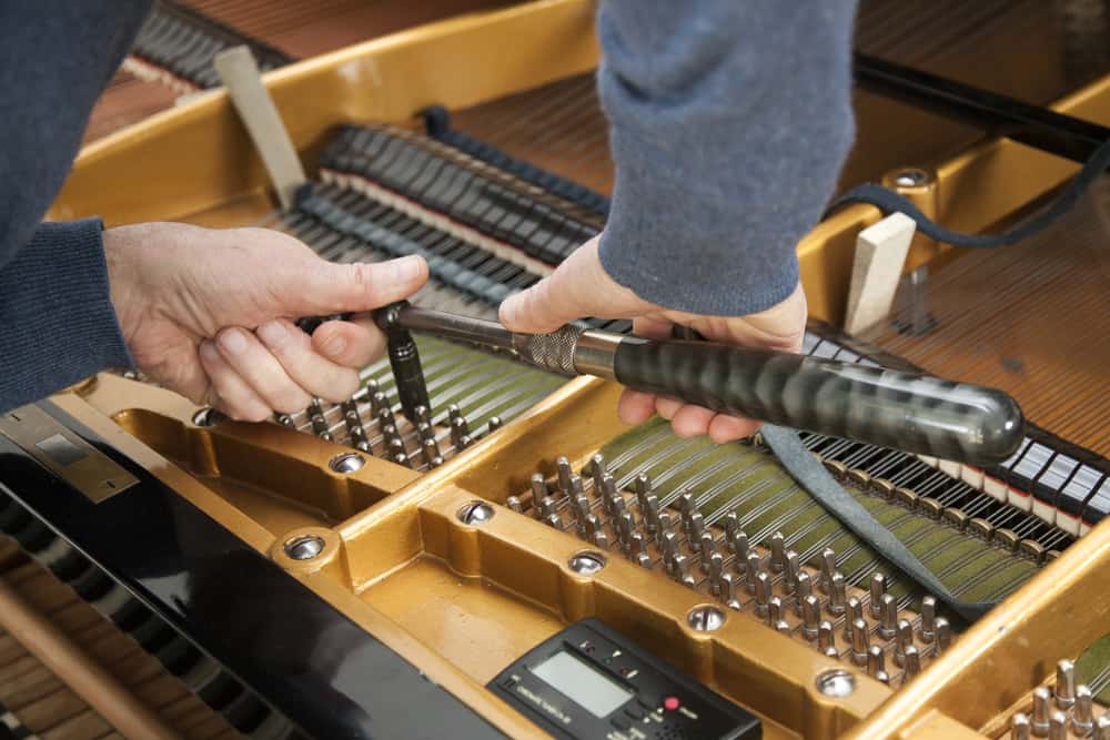 Hand and tools of tuner working on grand piano