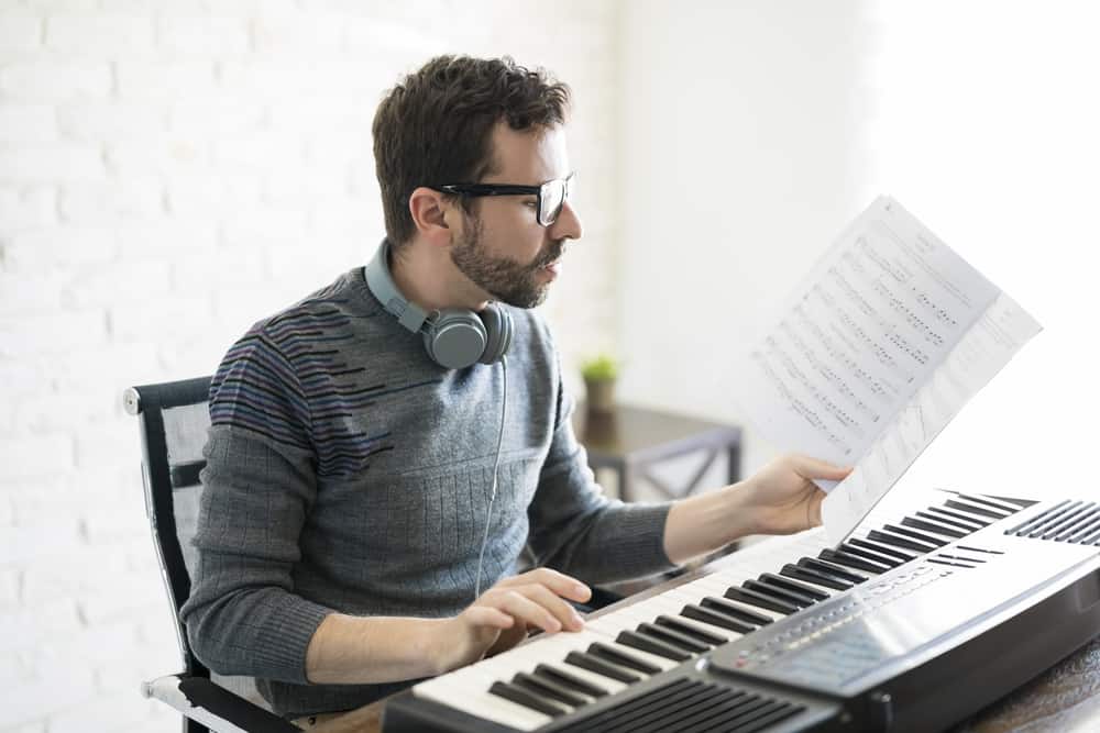 Handsome young man reading music sheet while playing piano