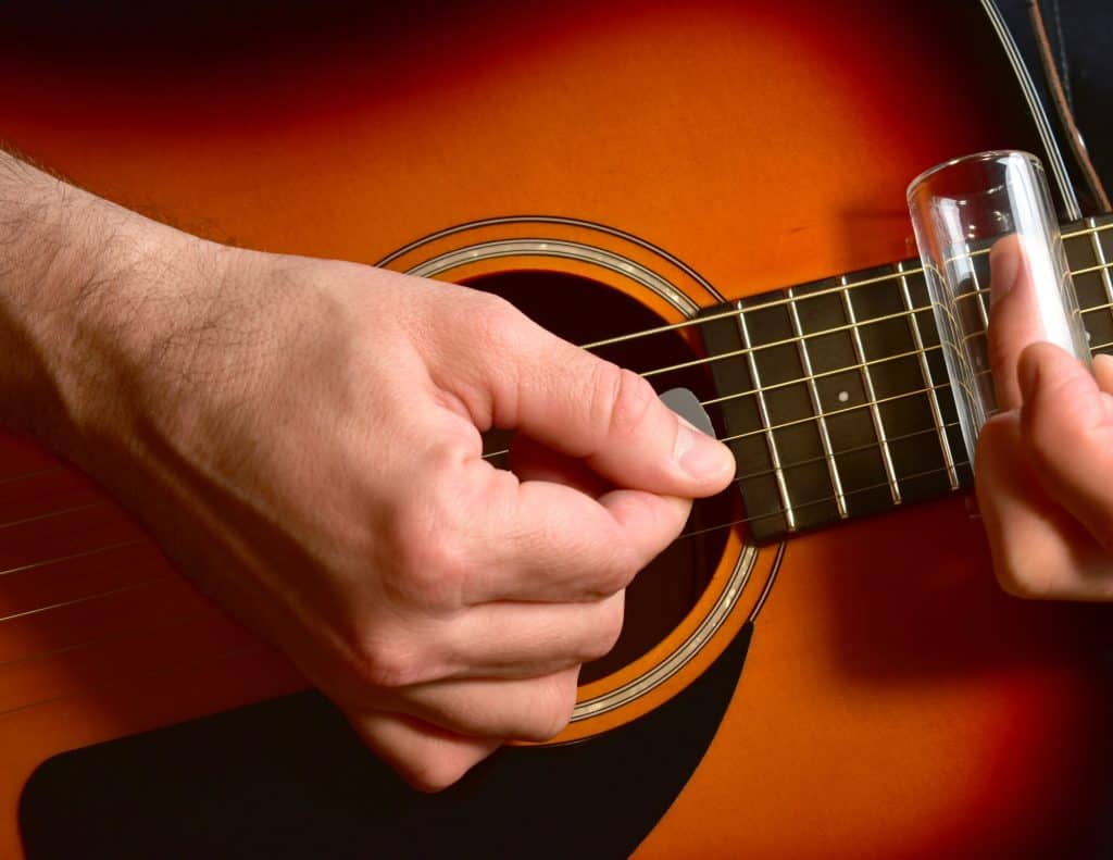 Man playing and acoustic guitar with a glass slide