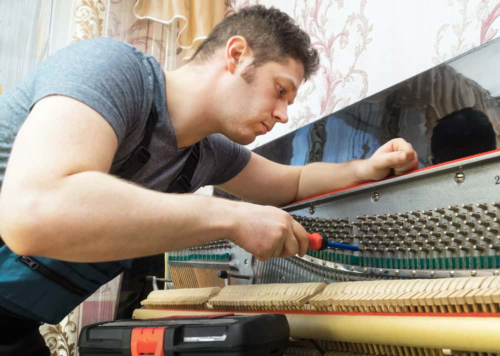 Professional piano technician tuning the piano with ratchet tool.