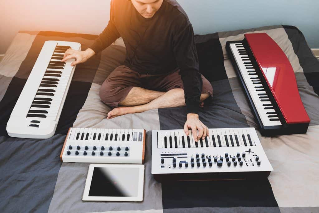 Songwriter playing music keyboards and piano on bed