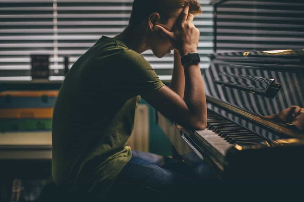 Teenager sitting at his piano with his head in his hands.