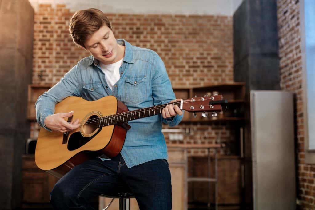 Young man sitting on a stool and playing a guitar