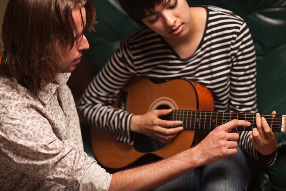 Young musician teaches student to play guitar